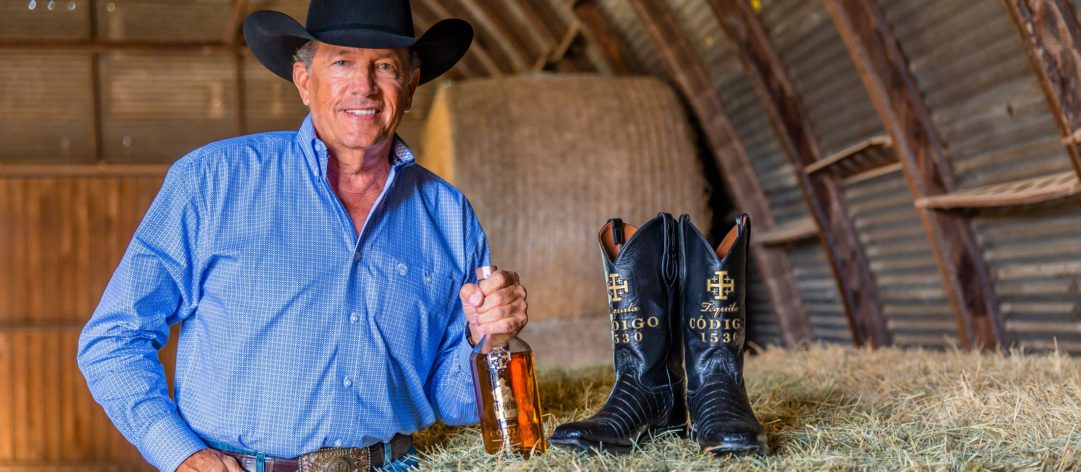 George Strait poses next to a hay bale with his Cotigo tequila.